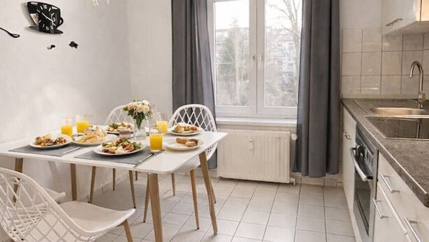 Une cuisine moderne avec des meubles blancs, une table à manger avec des chaises et une fenêtre avec des rideaux.