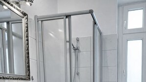 Une salle de bain moderne avec une douche à parois de verre, un lavabo blanc doté d’un distributeur de savon et des toilettes avec une fenêtre au-dessus.