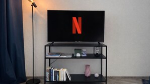 Un salon moderne avec un téléviseur à écran plat fixé sur un meuble noir, un lampadaire et une bibliothèque contenant des livres et des objets décoratifs.