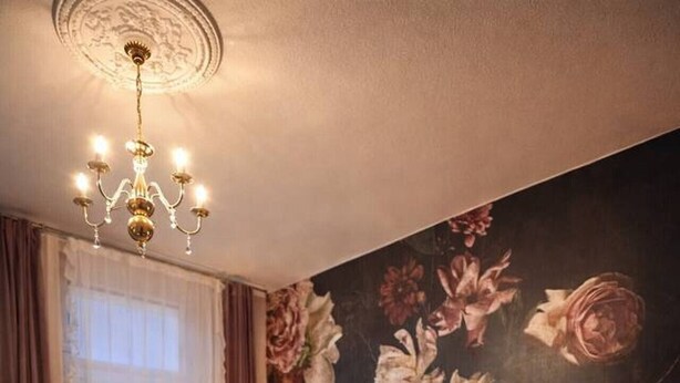 Un grand lit avec une tête de lit sombre, une fresque murale à motifs floraux et un lustre.
