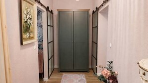 Un couloir doté d’un plancher en bois, d’un banc rose, d’une armoire verte et d’un lustre.