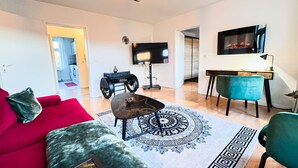 Een moderne woonkamer met een rode bank, een salontafel, een vloerkleed met dessin, een televisie en een bureau met stoel.