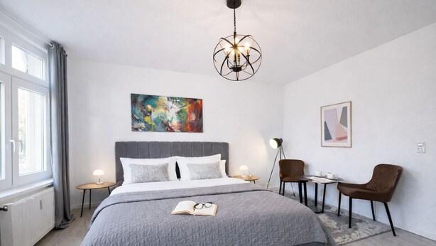 Ein modernes Hotelzimmer mit einem großen Bett, einem Schreibtisch, zwei Sesseln, einer Stehlampe und Bildern an den Wänden.