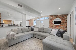 Un saló modern amb un sofà modular, una zona de cuina i una paret decorada amb maons.