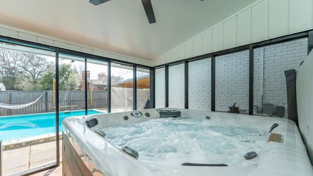 A hot tub in a room with large windows, a pool outside, and a ceiling fan. - Pool + Hot Tub Retreat · Sleeps 18 · Near Destin (Fort Walton Beach)