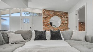 A modern bedroom with a large bed, grey sofas, a brick wall, and a round mirror. - Pool + Hot Tub Retreat · Sleeps 18 · Near Destin (Fort Walton Beach)