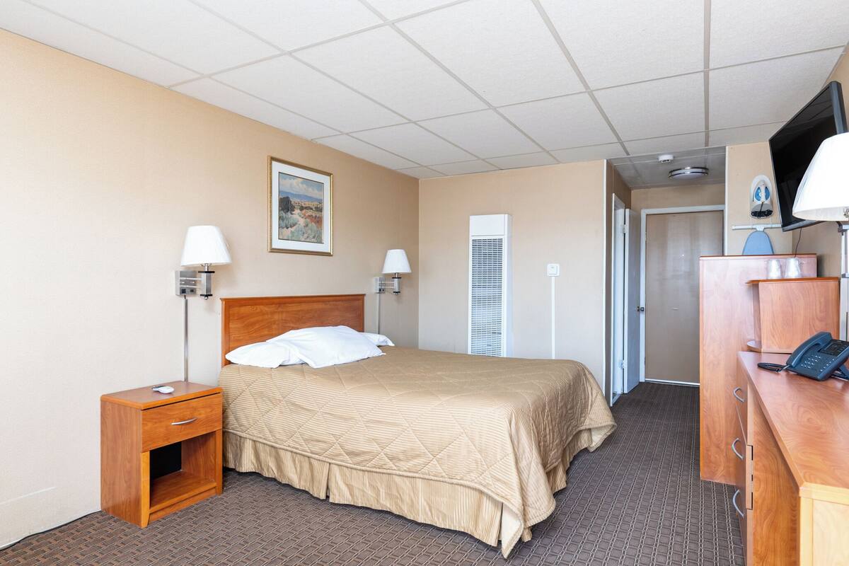A hotel room with a bed, bedside lamps, a desk with a phone, and a TV.