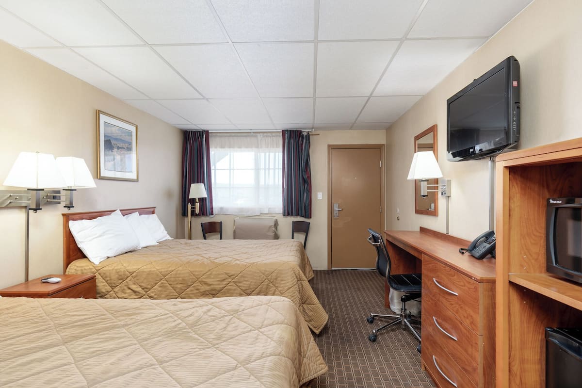 A hotel room with two beds, a desk, a television, and a bathroom.