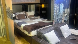 Quarto com cama, sofá, vista para a cidade e piso de madeira.