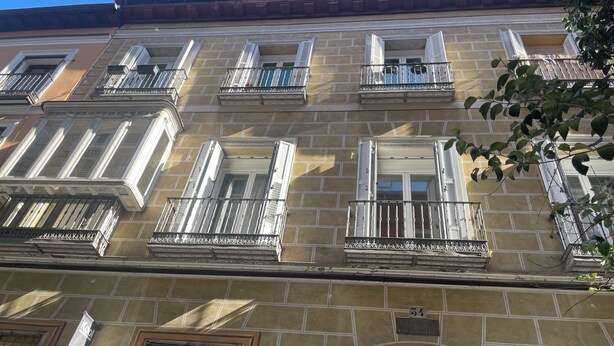 Um edifício com vários andares, varandas, uma entrada em arco destacada e uma placa com o número do prédio.