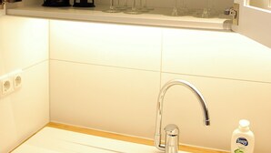 A kitchen with a sink, a faucet, a soap dispenser, and a shelf with cups and glasses. - Peaceful 1-bedroom studio in charming Enschede perfect for Short-Stay (Enschede)