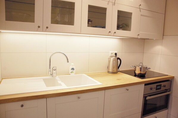 A kitchen with a wooden countertop, a sink, a kettle, and a stove.