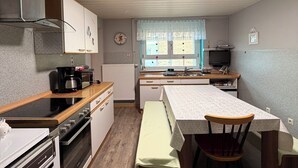 A compact kitchen with a stove, oven, and microwave. There is a dining table with chairs and a bench. A television is on a stand near the window. - Large family vacation apartment near Europapark - feel like at home (Meißenheim)
