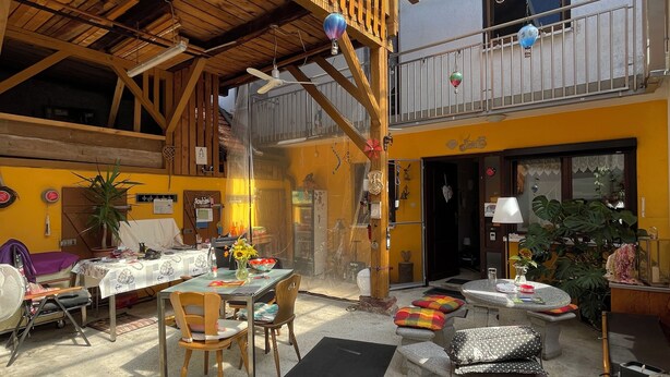 A spacious indoor area with a high ceiling, wooden beams, and a glass roof. There are tables and chairs arranged for dining, and a small balcony with a railing. - Large family vacation apartment near Europapark - feel like at home (Meißenheim)