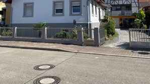 A white two-story house with a red roof, a gated driveway, and a small garden area. - Large family vacation apartment near Europapark - feel like at home (Meißenheim)