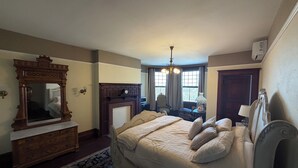 A bedroom with a large bed, a dresser, a mirror, a fireplace, and a chandelier. - Beautiful Historic Mansion, located in Cornwall, PA (Lebanon)