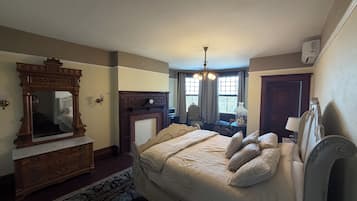 A bedroom with a large bed, a dresser, a mirror, a fireplace, and a chandelier.