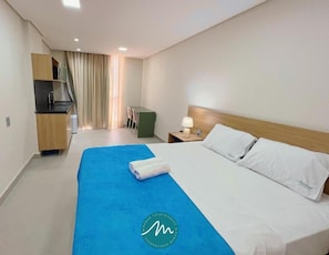A hotel room with a bed, a desk, a chair, and a kitchenette. - Acqua Tambaú (João Pessoa)