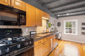 A kitchen with wooden cabinets, a black microwave, a stove, and a window with a view.