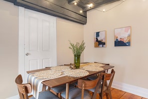 A dining area with a wooden table, chairs, a vase with flowers, and two abstract paintings on the wall.