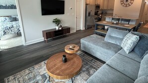 Ein modernes Wohnzimmer mit einem grauen Modulsessel, einem Holztisch und einem an der Wand befestigten Fernseher.