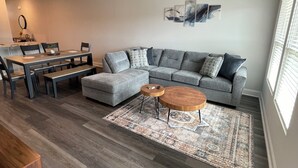 Ein modernes Wohnzimmer mit einem grauen Ecksofa, einem Holztisch und einem gemusterten Teppich.