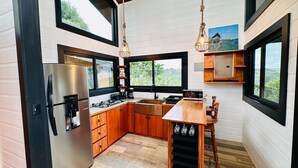 A modern kitchen with a stainless steel refrigerator, wooden cabinets, a wooden countertop, and a bar area with hanging wine glasses.