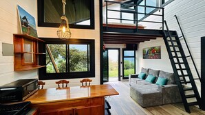 A modern kitchen with a wooden island, a dining area, a gray sofa with teal cushions, and a staircase to an upper level.