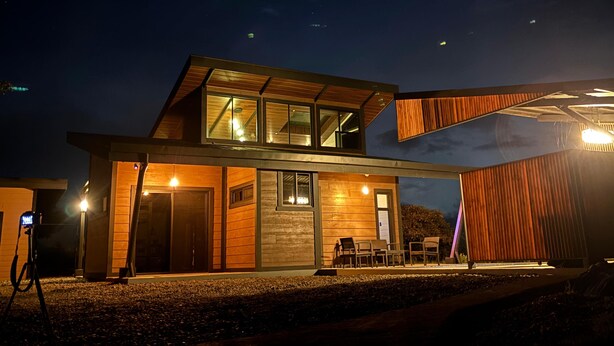 A modern two-story house with a large glass window and a wooden deck.