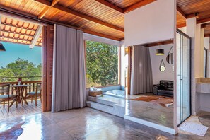 Interior moderno com teto de madeira, porta de vidro que dá para área externa, banheira e zona de estar com mesa e cadeiras.
