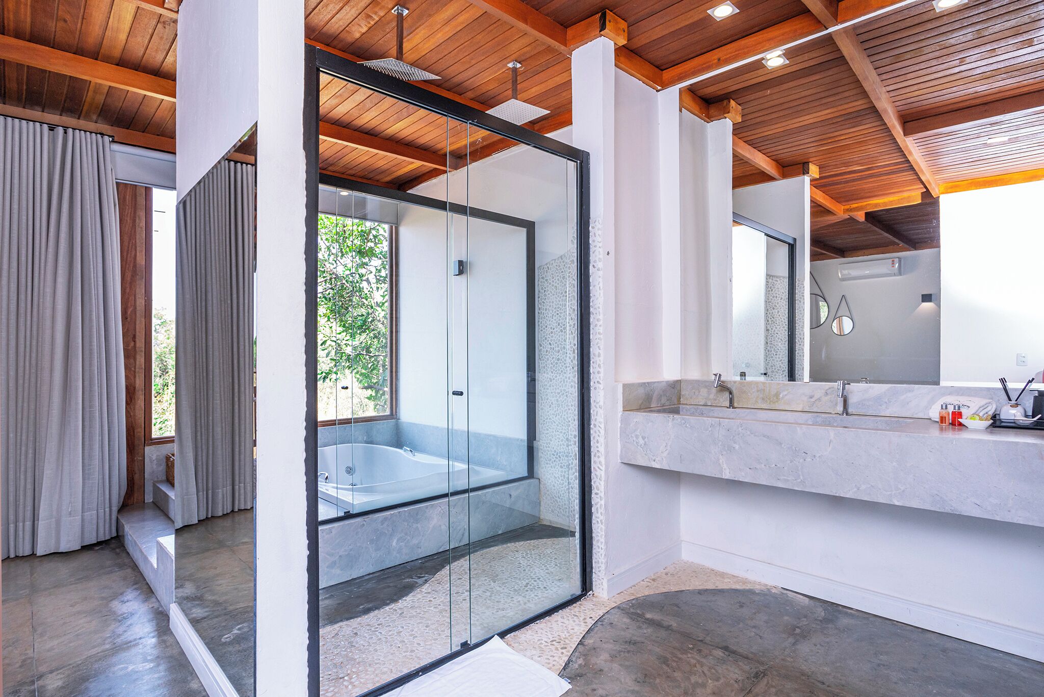 A modern bathroom with a glass-enclosed shower, a marble countertop, and wooden ceiling beams.