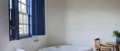 Un baño con una bañera, un banco de madera, una silla, una mesita con una planta y baldosas de suelo estampadas.