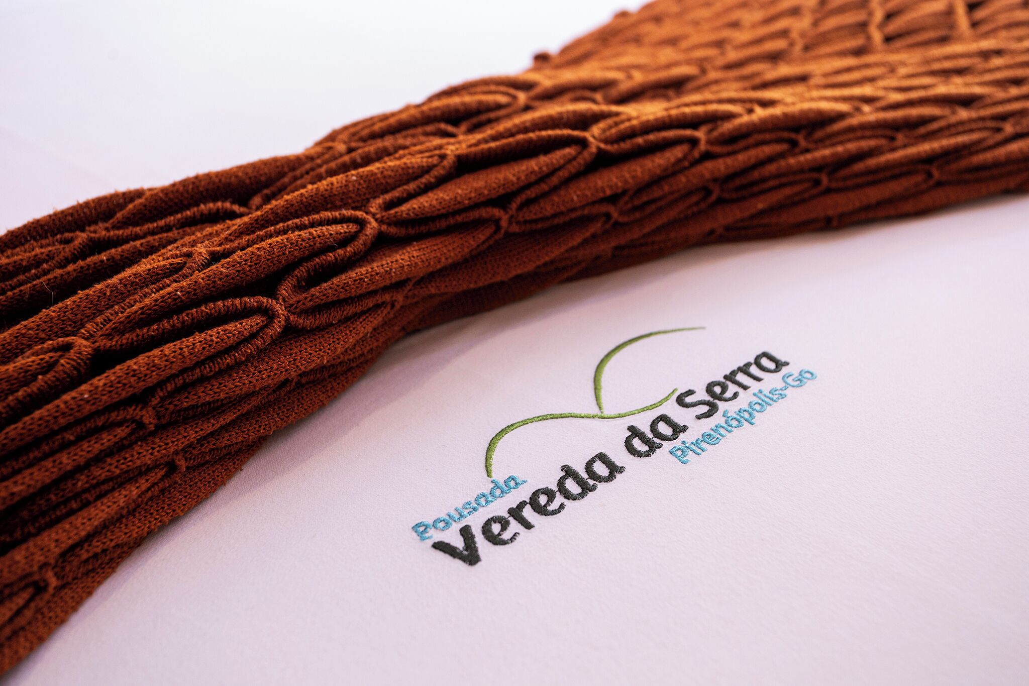 A close-up of a brown braided fabric with the text 'Pousada Vereda da Serra' and 'Pinhões, Go' on a white background.