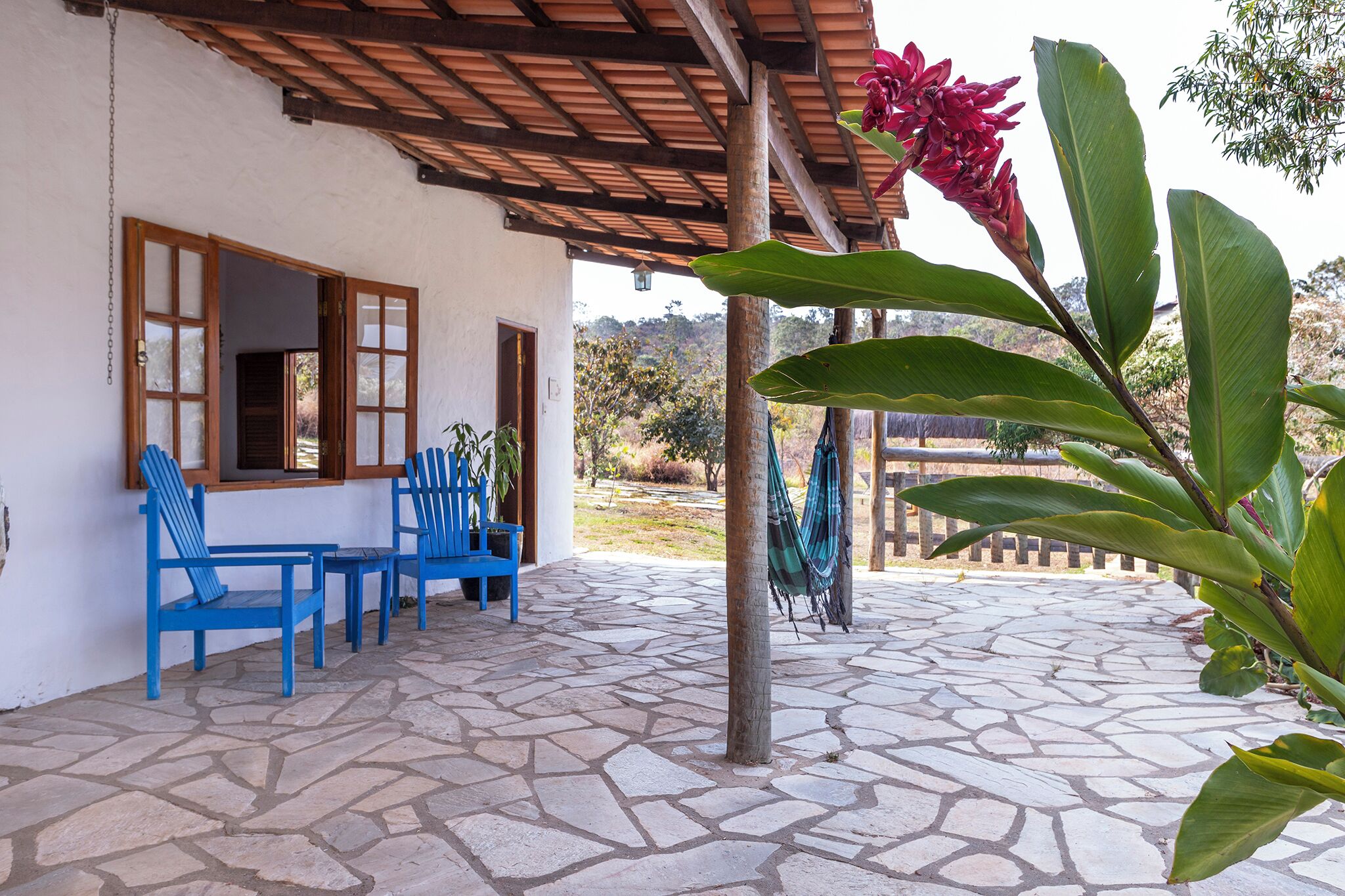 A covered patio with stone flooring, blue chairs, and a hammock.