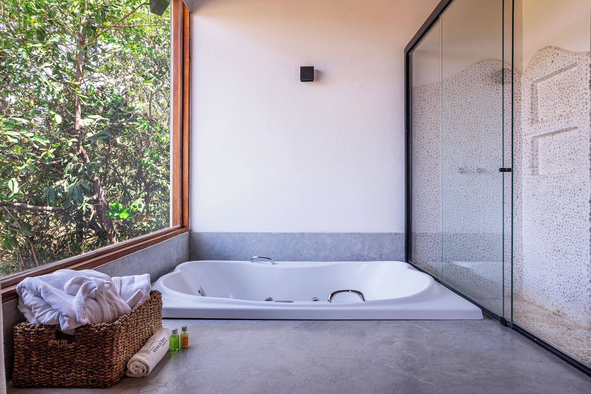 A modern bathroom with a freestanding bathtub, a glass shower enclosure, and a view of greenery through a window.
