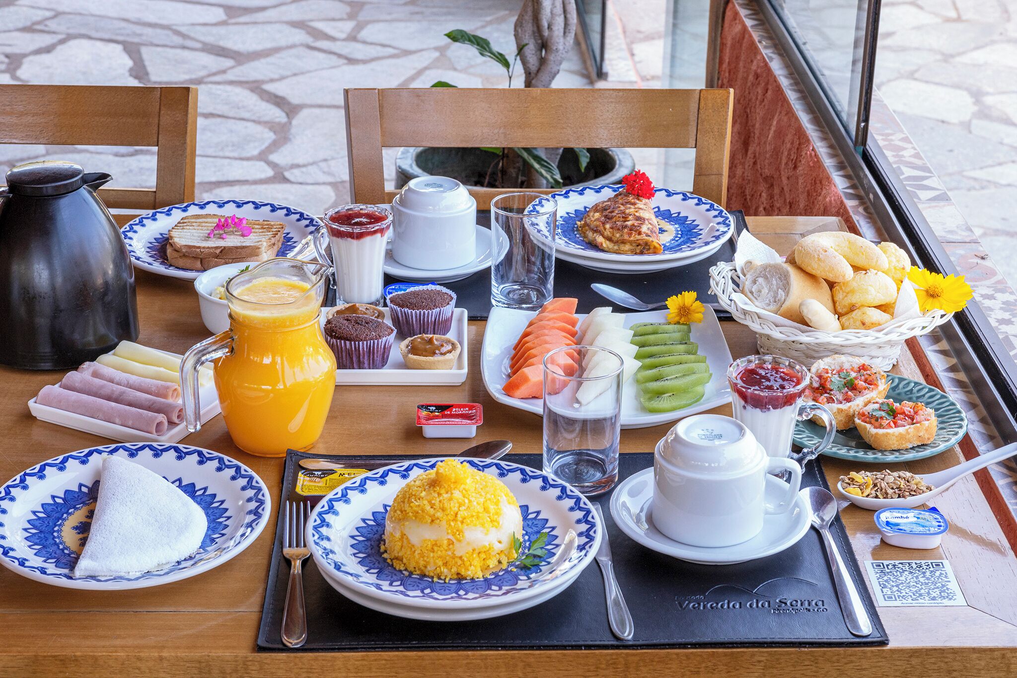 Una mesa de desayuno con platos de comida, una cafetera y una jarra de jugo de naranja.