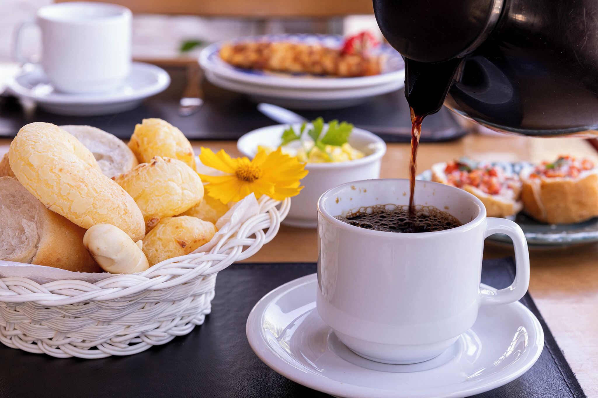 Una taza de café sobre un plato con una cesta de pan y una flor a un lado.