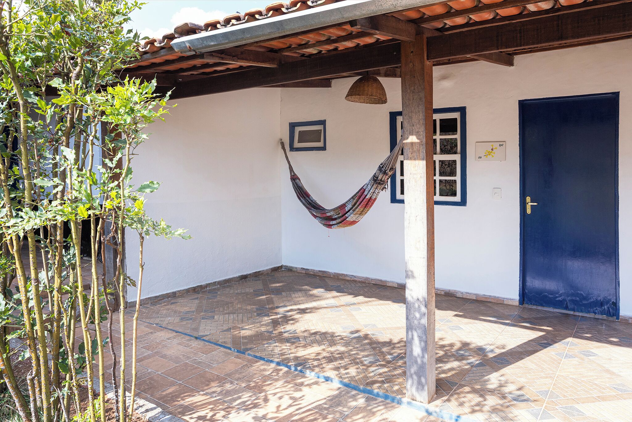 Un espace extérieur abrité, avec un hamac, une porte bleue et un sol carrelé.