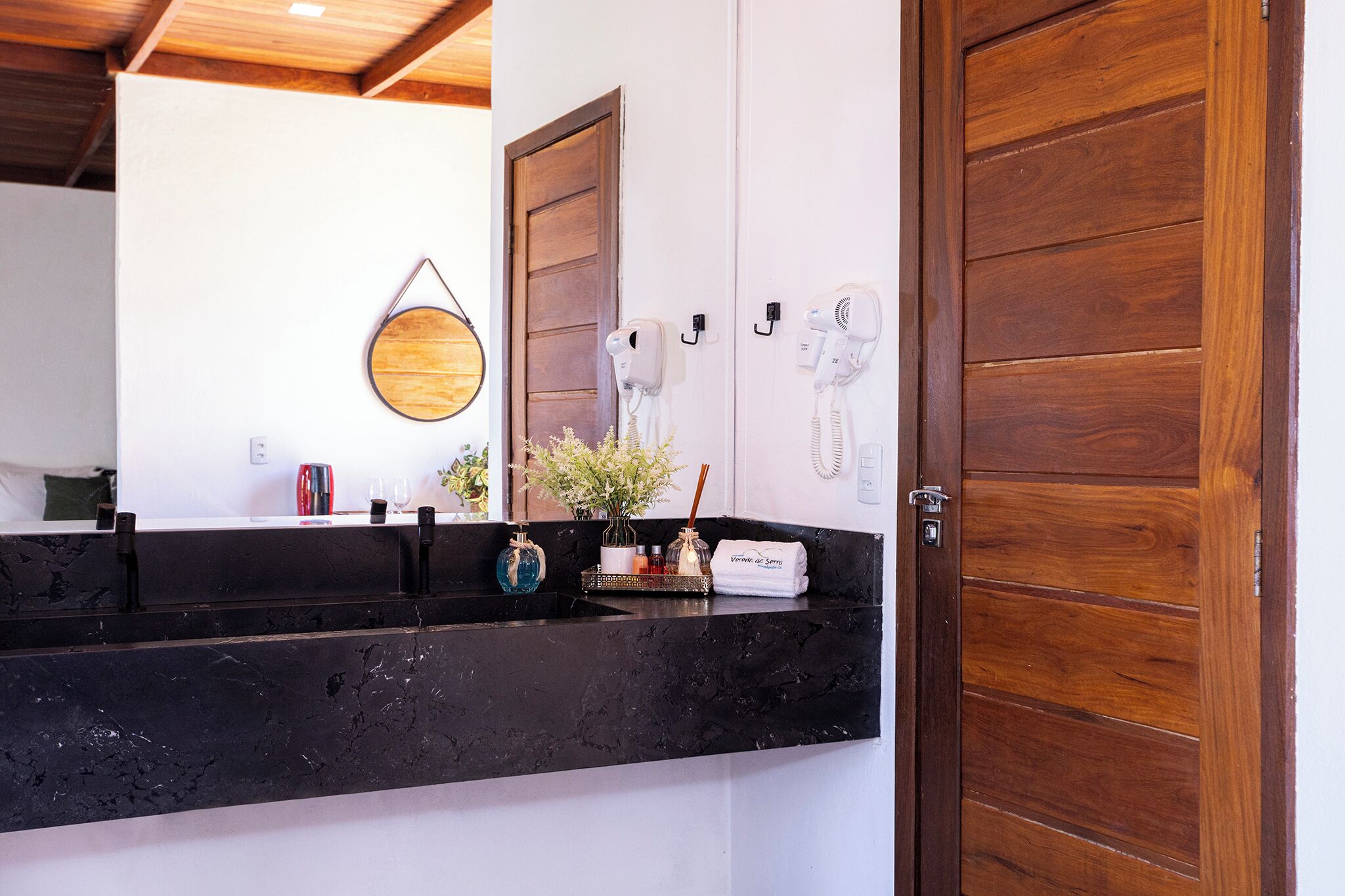 A bathroom with a black marble countertop, a wooden door, and two hair dryers mounted on the wall.