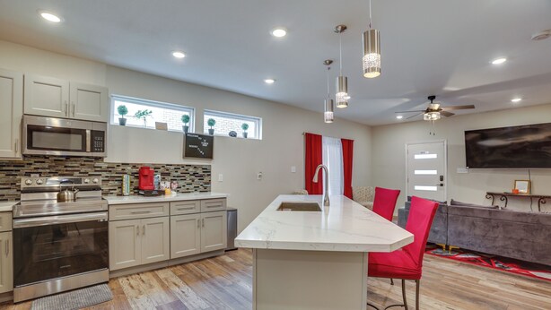A modern kitchen with a central island, stainless steel appliances, and a dining area with red chairs. - Sleek & Central! Houston Stay Near Med Center (Houston)