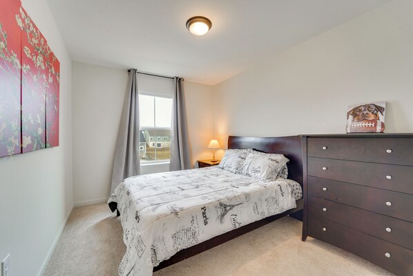 Un dormitorio con cama, cómoda, lámpara y ventana con cortinas.