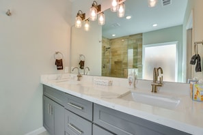 Une salle de bain avec un grand miroir, deux lavabos et une douche.