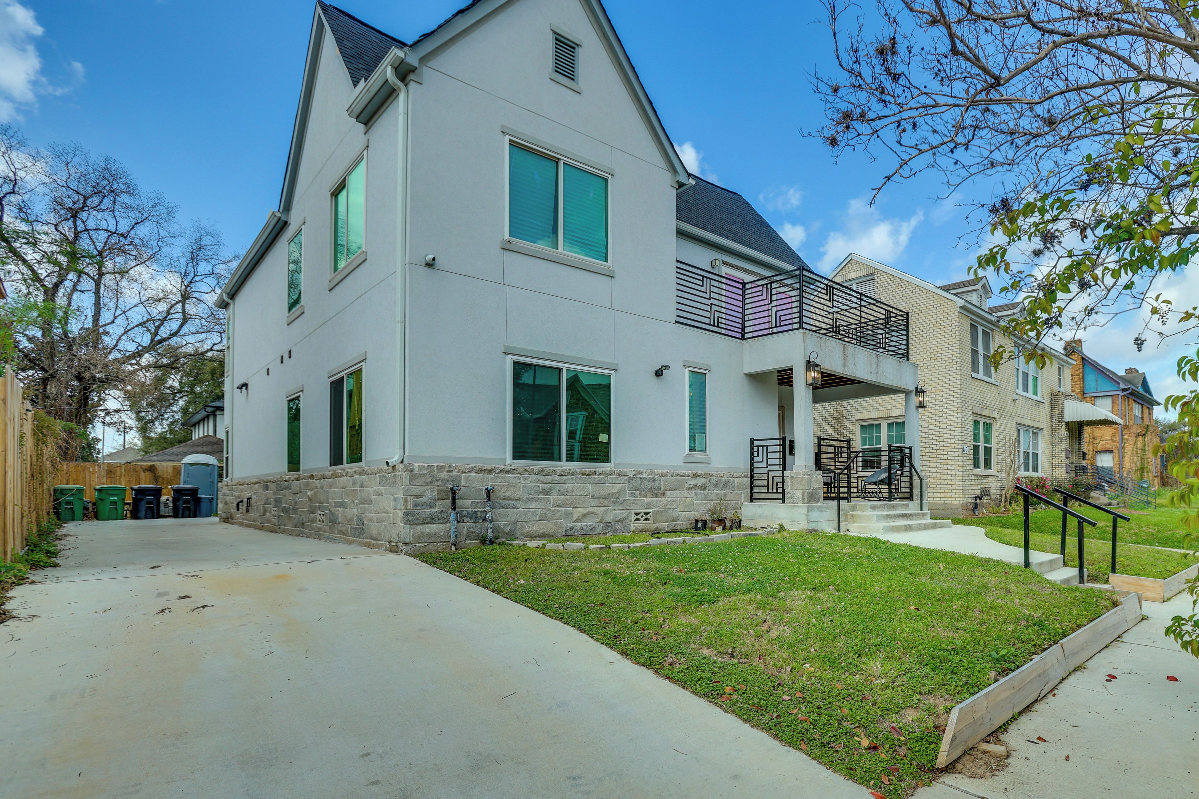 A modern two-story house with a stone foundation, large windows, and a balcony with a black railing.