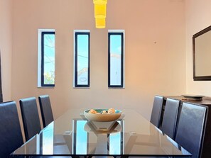 A conference room with a glass table, black chairs, a bowl of snacks, and three windows with views.