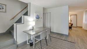 A modern interior with a staircase, a desk with a chair, a patterned rug, and a door leading to another room. - Work, Relax & Explore The 'Burgh! McKeesport Home (McKeesport)