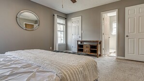 Un dormitori amb un llit, un ventilador de sostre, un mirall rodó, un taulell i una porta que dona a una altra habitació.