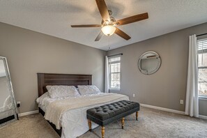 Un dormitorio con cama, ventilador de techo, espejo redondo y ventana.