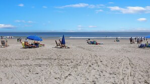 Una playa con tumbonas y sombrillas, cielo despejado y el océano al fondo.