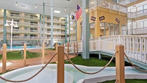 Interior de un hotel de varios niveles con balcones, una zona de piscina y señalización que indica habitaciones y áreas de juegos.