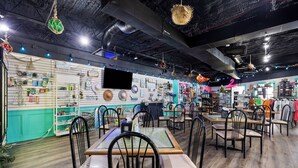 Un restaurante con varias mesas y sillas, una pantalla de televisión y diversas decoraciones colgantes.